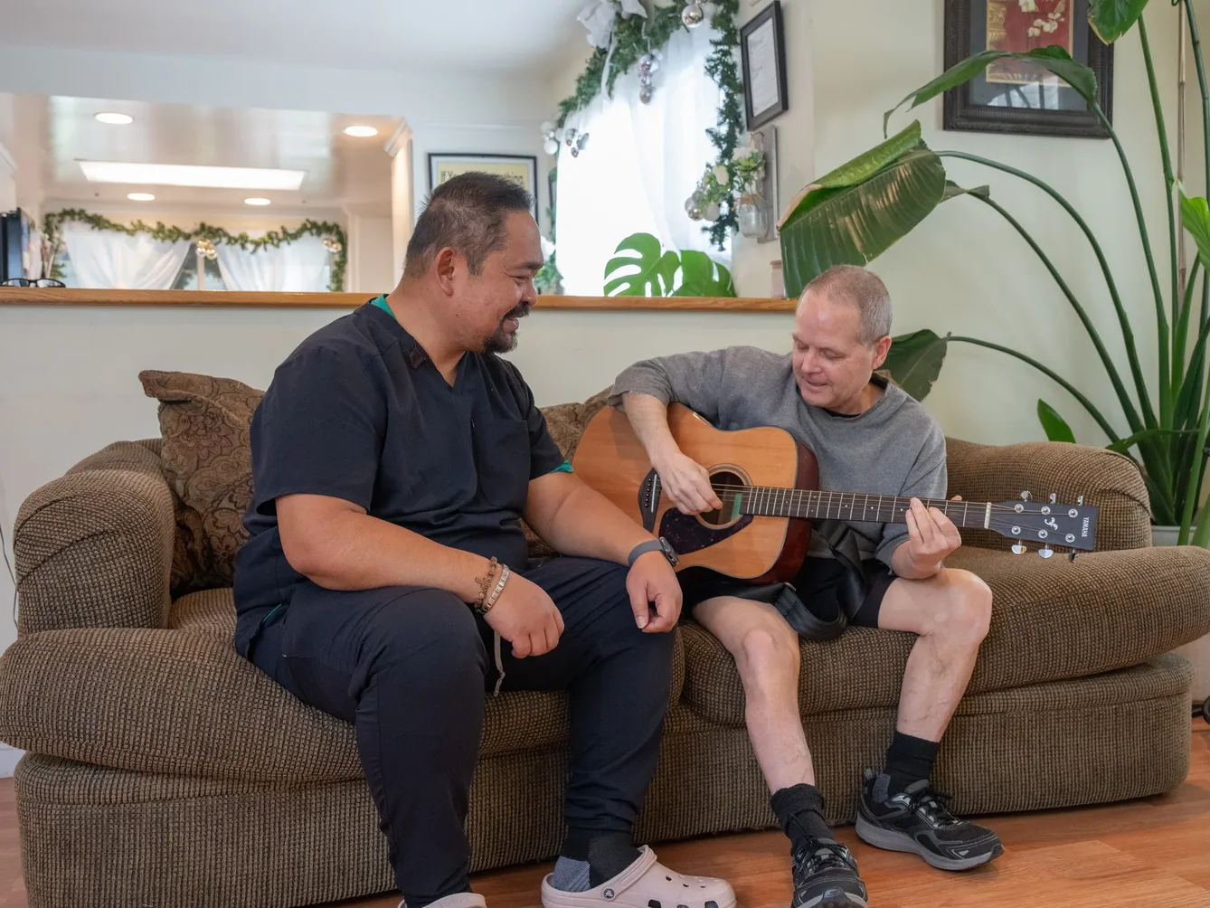 Caregiver and resident enjoying music therapy session together on living room couch