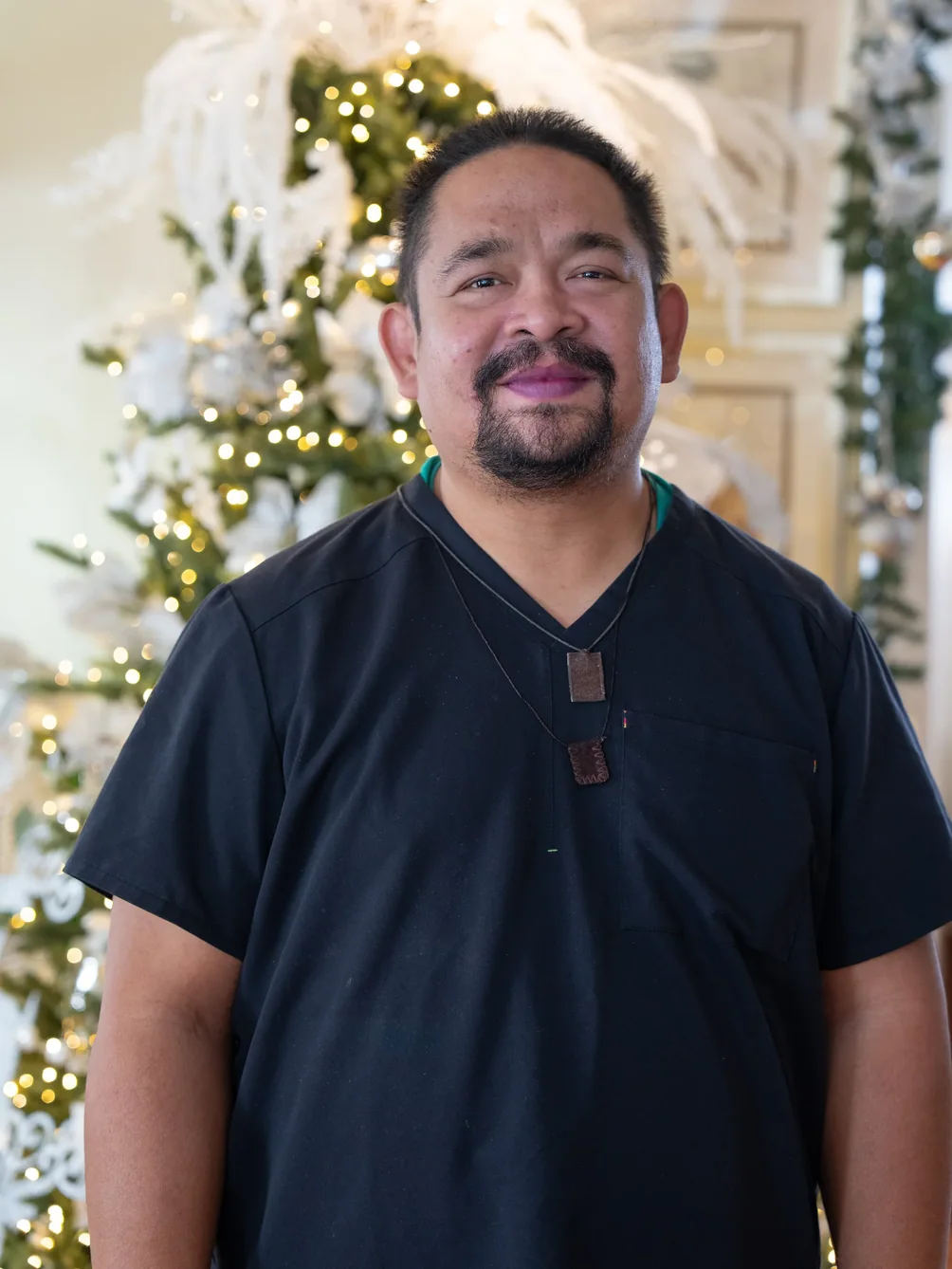 Smiling male caregiver in dark scrubs standing in festive holiday-decorated home environment